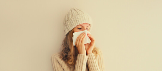 Sick upset woman sneezing blow nose using tissue wearing warm soft knitted clothes, hat and sweater...