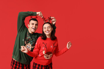 Happy young couple in Christmas pajamas on red background