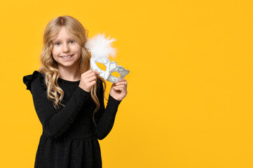 Funny little girl with carnival mask on yellow background