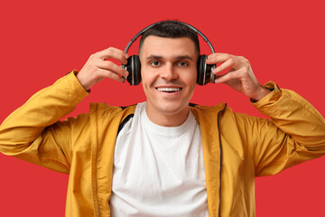 Young man in stylish jacket and headphones on red background