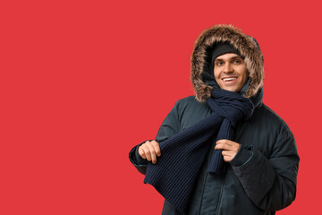Young man in stylish puffer jacket and scarf on red background