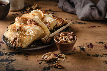 Crepes or thin pancakes with honey and nuts on brown plate over wooden background. Delicious...