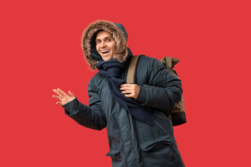 Young man in stylish puffer jacket and scarf with bag on red background