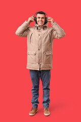 Young man in stylish puffer jacket and headphones on red background