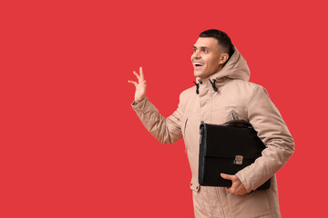 Young man in stylish puffer jacket with bag on red background
