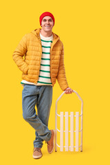 Young man in stylish puffer jacket with sled on yellow background