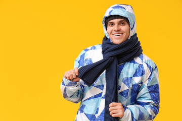 Young man in stylish puffer jacket and scarf on yellow background