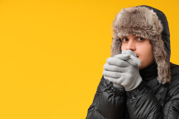 Young man in black stylish puffer jacket and hat on yellow background