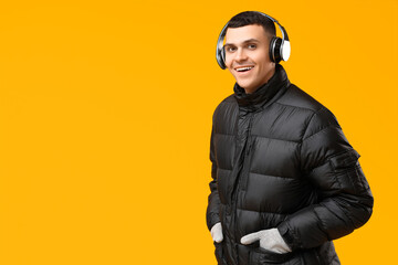 Young man in black stylish puffer jacket and headphones on yellow background