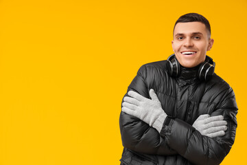 Young man in black stylish puffer jacket and headphones on yellow background