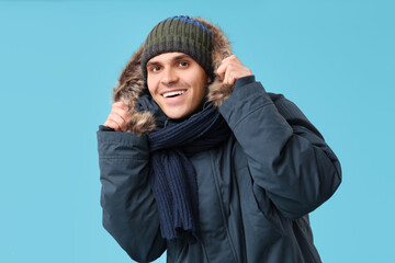 Young man in stylish puffer jacket and scarf on blue background