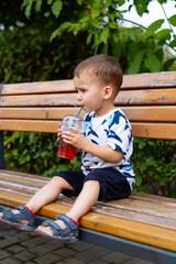 A little boy sitting on a bench drinking a drink. The Curious Little Boy Enjoying a Refreshing...