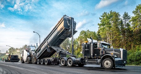 Semi-trailer truck unloading asphalt into a material transfer vehicle during paving of the...