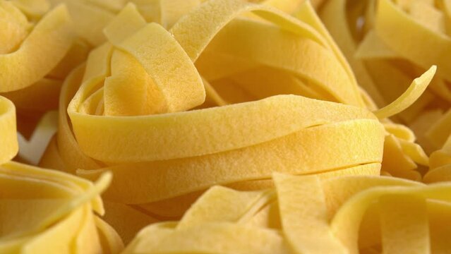 Uncooked italian pasta Tagliatelle or Fettuccine macro rotating background for advertising side light. Durum wheat pasta or macaroni
