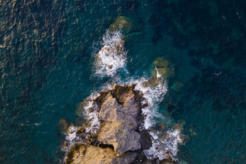 Aerial view of Sea waves crashing and white foaming on empty big rock stones seashore. Wild sea washing reef rock cliff