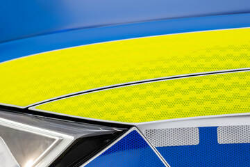 Generic police emergency vehicle car hood reflective light yellow blue white finish stickers full frame object detail up close. Simple emergency response services symbol, background texture, nobody