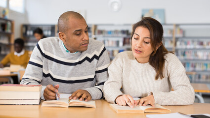 Young adult people studying together in library, talking, reading books and writing in notepads