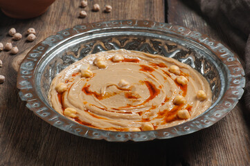 High angle photo of humus in a traditional copper plate with raw chickpeas and flat breads in the background
