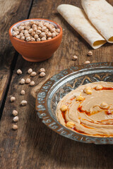 High angle photo of humus in a traditional copper plate with raw chickpeas and flat breads in the background