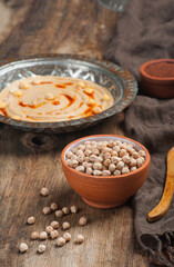 High angle photo of a bowl of raw chickpeas with a humus plate in the background