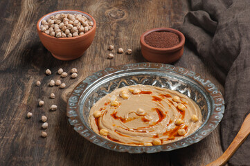 High angle photo of humus in a traditional copper plate with raw chickpeas and flat breads in the background
