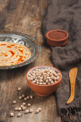 High angle photo of a bowl of raw chickpeas with a humus plate in the background