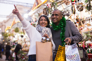 Happy married couple point finger at selected christmas tree decorations at street market