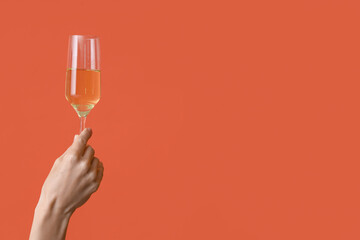 Female hand with glass of champagne on orange background