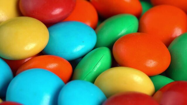 Sweet dragees in colored glaze are rotating background macro front light. Delicious sweets and candies close-up that children like. Chocolate Coating