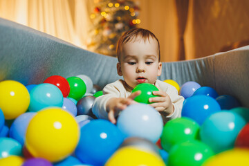 A cute little boy is playing in a pool of plastic balls. Children's dry pool at home.