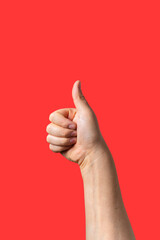 Close-up of a male arm doing thumb up sign isolated on red background
