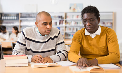 Portrait of two adult men engaged in research, looking together for information in books in library