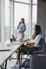 Two young women work in a modern office. Work office space with large windows. Woman manager works at the desk sitting in the office.