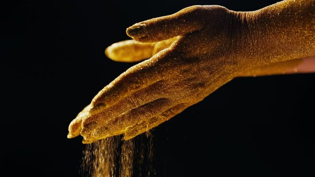 Golden glittering woman hands with dust, sand on black background. Life moments.