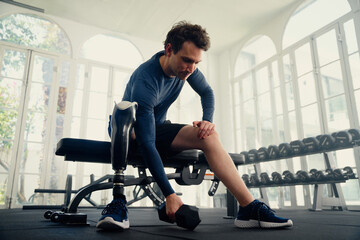 Fototapeta na wymiar Young caucasian man with prosthetic leg doing weight training exercises with dumbbell at the gym