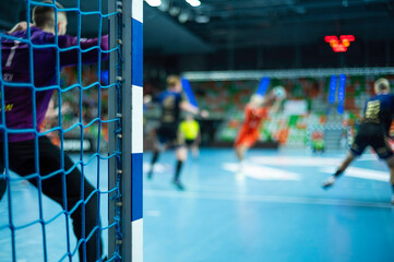 Detail of handball goal post with net and handball match in the background.