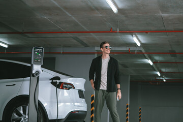 Young man travel with EV electric car to shopping center parking lot charging in downtown city...