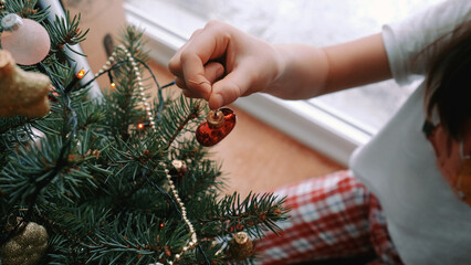 Hand of girl touching pine cone hanging on Christmas tree at home