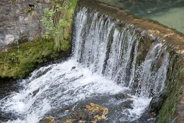 Fototapeta premium A small waterfall created by a concrete dam at the source of Krupajsko vrelo. Close up, movement, water flowing.