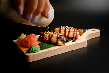 Sprinkle sesame on a two pieces of fish on a thick wooden board