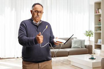 Confused mature man holding a router at home - obrazy, fototapety, plakaty