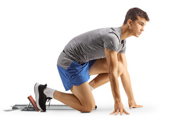 Full length profile shot of a male teenage athlete kneeling on running start blocks