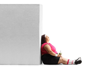 Corpulent woman in sportswear holding a smoothie and leaning on a wall