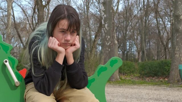 Depressed teen on children carousel. A lonely teen girl sitting with sad emotions on carousel in the city park.