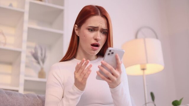 Attractive young red haired woman at home get notification and feeling upset reading bad negative news message on smartphone and looking at screen indoors Disappointment Fail Unemployment