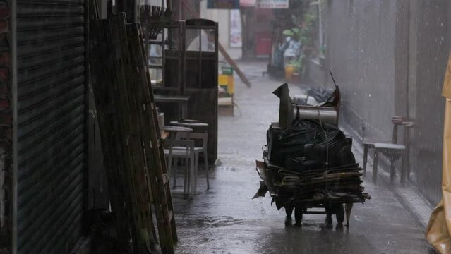 Hard rain falls in slow motion on cardboard stacked on cart in alley
