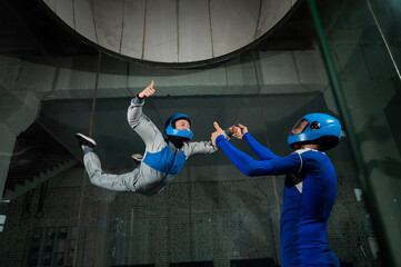 A male instructor teaches a woman how to fly in a wind tunnel. Free fall simulator.