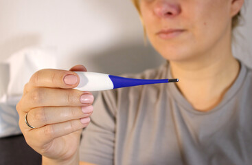 Close up of sick woman looking at electronic thermometer, blurry background