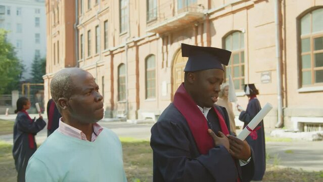 Tracking shot of African American graduated son talking to his middle-aged father about university