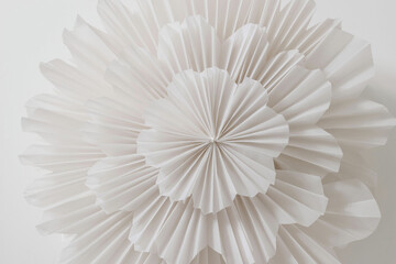 Detail of folded paper decoration, garland for party, new year, bachelorette, birthday or carnival isolated on table background. White, round floral or snowflake shaped rosette. Winter decoration.